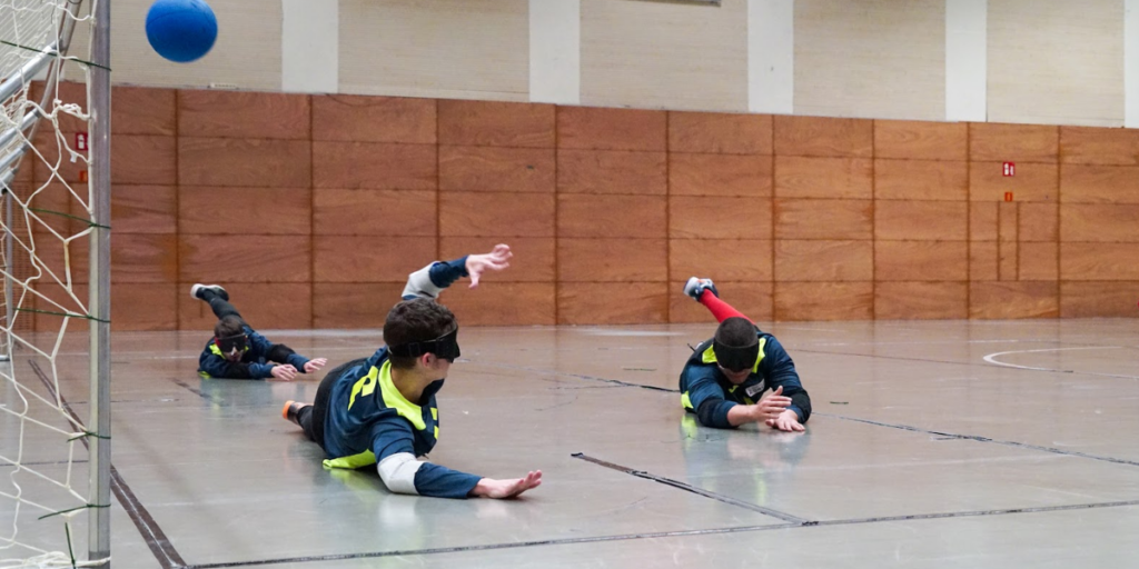 Tres esportistes de goalball estirats a la porteria, preparats per aturar una pilota durant un partit.